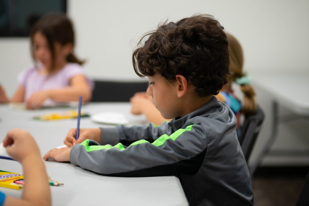 Children writing at a classroom table.