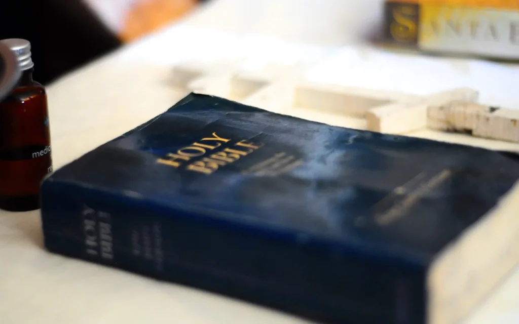 Holy Bible on table with cross and bottle.